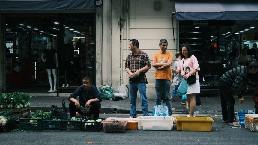 Feira de rua movimentada em São Paulo, com pessoas circulando entre bancas de produtos frescos.