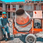 Trabalhador da construção civil opera uma betoneira num estaleiro de obras, usando equipamento de proteção.