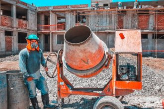 Trabalhador da construção civil opera uma betoneira num estaleiro de obras, usando equipamento de proteção.