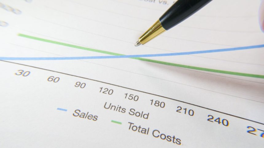 Caneta apontando para um gráfico financeiro com linhas de vendas e custos.