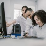 Grupo diverso de cientistas trabalha em conjunto diante de um computador em um laboratório moderno.
