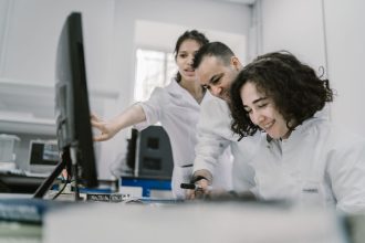 Grupo diverso de cientistas trabalha em conjunto diante de um computador em um laboratório moderno.