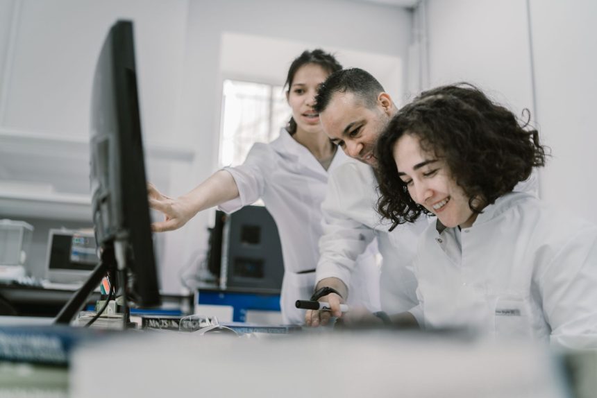 Grupo diverso de cientistas trabalha em conjunto diante de um computador em um laboratório moderno.