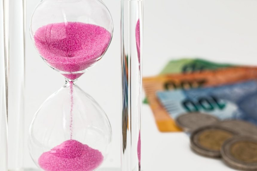 Ampulheta sobre moedas e cédulas, representando espera e questões financeiras.
